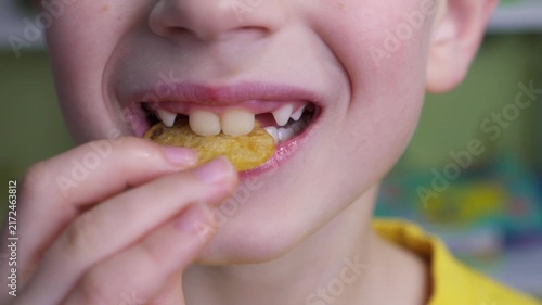 Seven-year-old boy puts a potato chip into his mouth in slow motion. Close framing captures his smile and missing baby teeth, portraying childhood snacking, tasty food, casual eating, and family life.