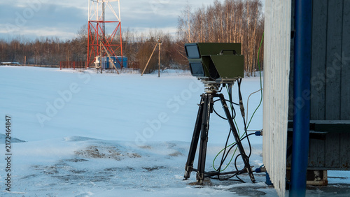 Obraz na płótnie In a secluded winter landscape, a radar system is strategically positioned beside a building, its equipment contrasting against the blanket of fresh snow carpeting the ground
