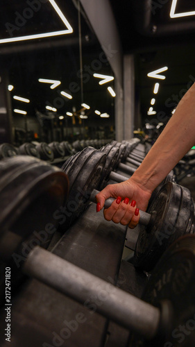 Cuadro en lienzo Woman's hand with red nails picking up a dumbbell in a gym