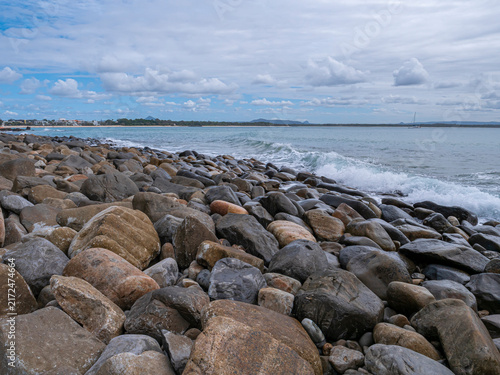 Obraz na plátně Waves crash against rocky shore under cloudy sky