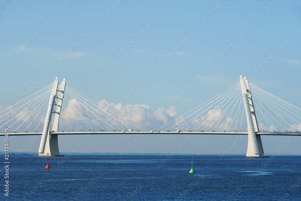 Fototapeta premium A modern cable-stayed automobile bridge spans the vast ocean under a clear blue sky.