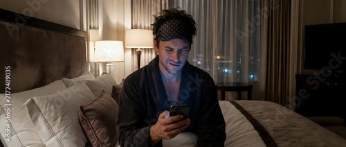 Man in bathrobe with headband checking smartphone in hotel room
