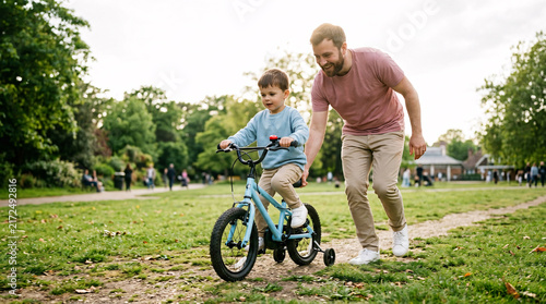 Father helping son learning to ride bicycle outdoors in park