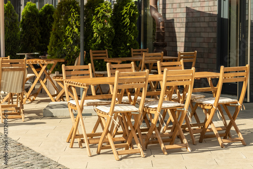 Canvastavla Empty outdoor cafe terrace with wooden tables and chairs in sunlight