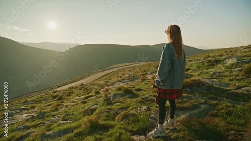 Person stands on a mountain slope looking at the sunset while wearing a denim jacket and black leggings