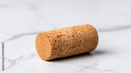A natural cork stopper lies on a white marble surface, showcasing its textured and porous material.
