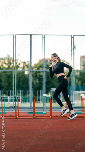 Foto Athletic woman in black sportswear running hurdles on a track during daytime