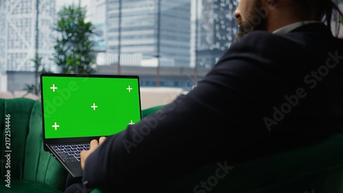 Canvas Print Young business leader looks at a green screen on a laptop in office space while managing corporate strategy profitability and an efficient work environment