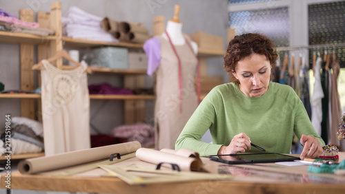 Foto Female dressmaker draw outline of future dress on paper while looking at the scr