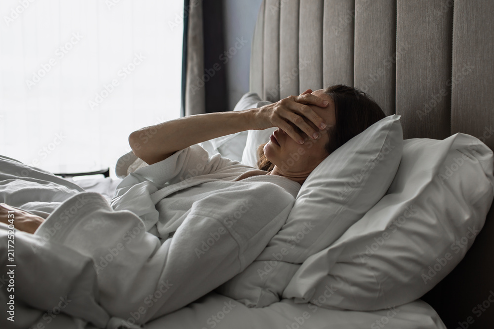 Fototapeta premium Tired Woman Waking Up in Bed Covering Her Face with Hand 