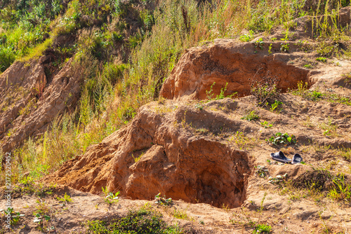Bild auf Leinwand A pair of abandoned rubber clogs rests beside a deep soil erosion hole in a rugg