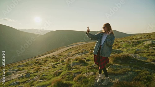 Person taking a selfie on a mountain with a sunset in the background near a winding road