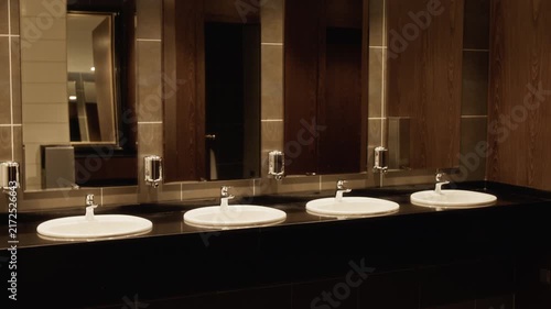 Camera panning across modern public restroom interior featuring row of sinks, large mirrors, and wooden panels. Ideal for hospitality marketing or commercial real estate promotions