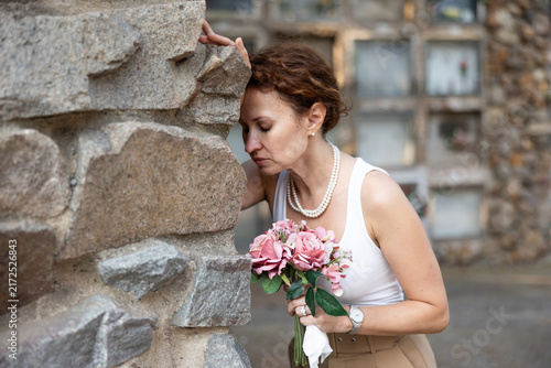 Фотография Middle aged woman in mourning, wearing white tank top and pearl necklace, leanin