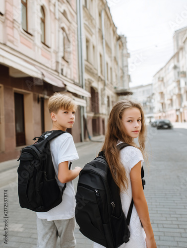 Zwei Schüler mit Rucksäcken auf dem Weg durch die Stadt blicken zurück. Schulweg, Freundschaft, Jugend, Bildung, Schulalltag, Teenager und moderner urbaner Lifestyle.