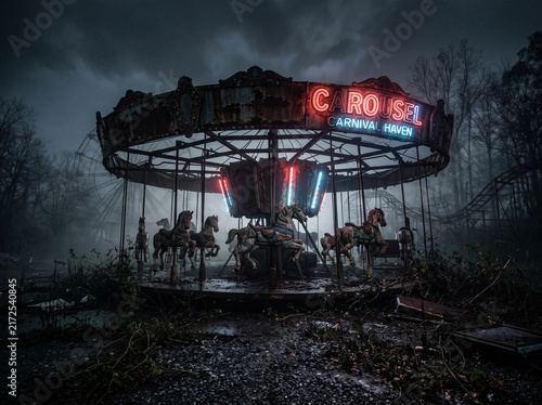 Eerie and abandoned amusement park carousel glowing with neon lights in a dark, foggy night setting