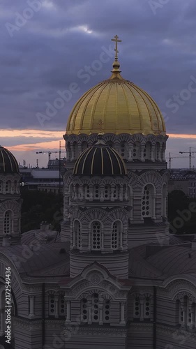 An aerial panning shot shows the golden domes and Byzantine revival architecture of the Nativity of Christ Cathedral in Riga, Latvia, at sunset.