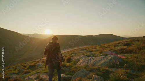 Mountains at sunset with a person hiking on a rocky path near a valley in the background