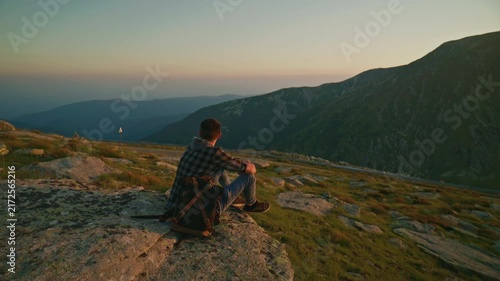 Man sits on a rock and looks at the mountains during sunset in a natural landscape