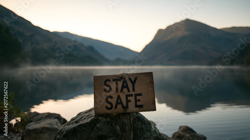 Stay safe wooden sign on rocks beside calm mountain lake.