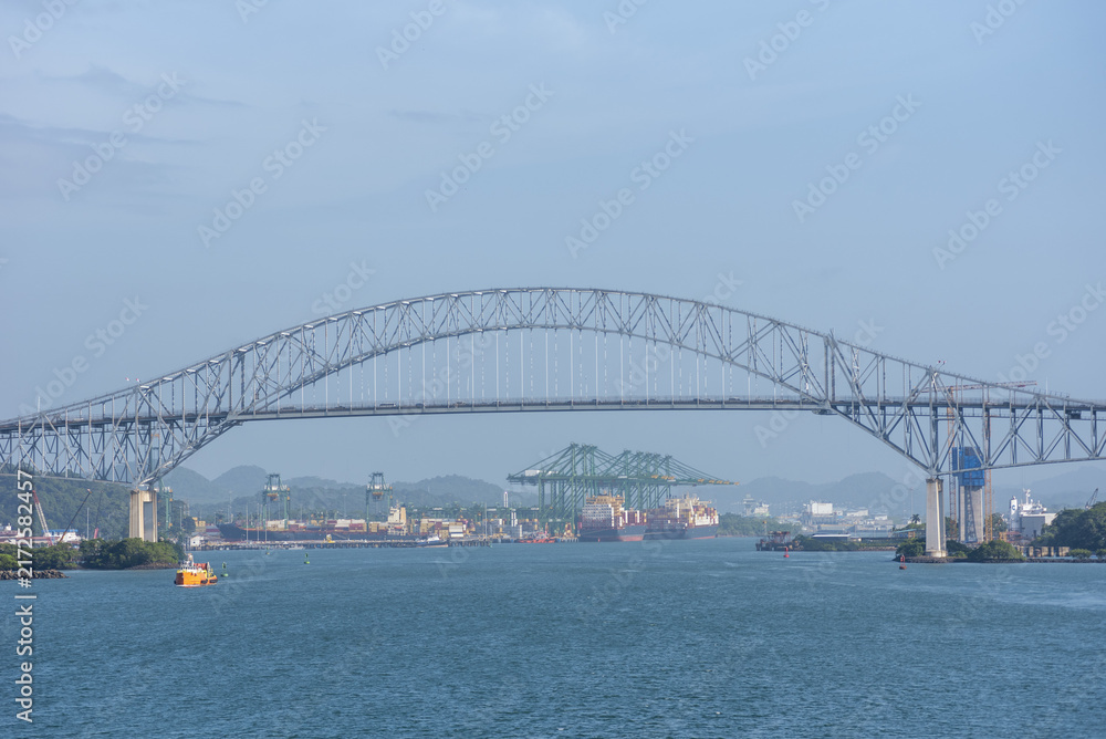 Fototapeta premium Scenic panorama of the Bridge of the Americas viewed from the ocean, with container ships and port infrastructure visible in the distance.