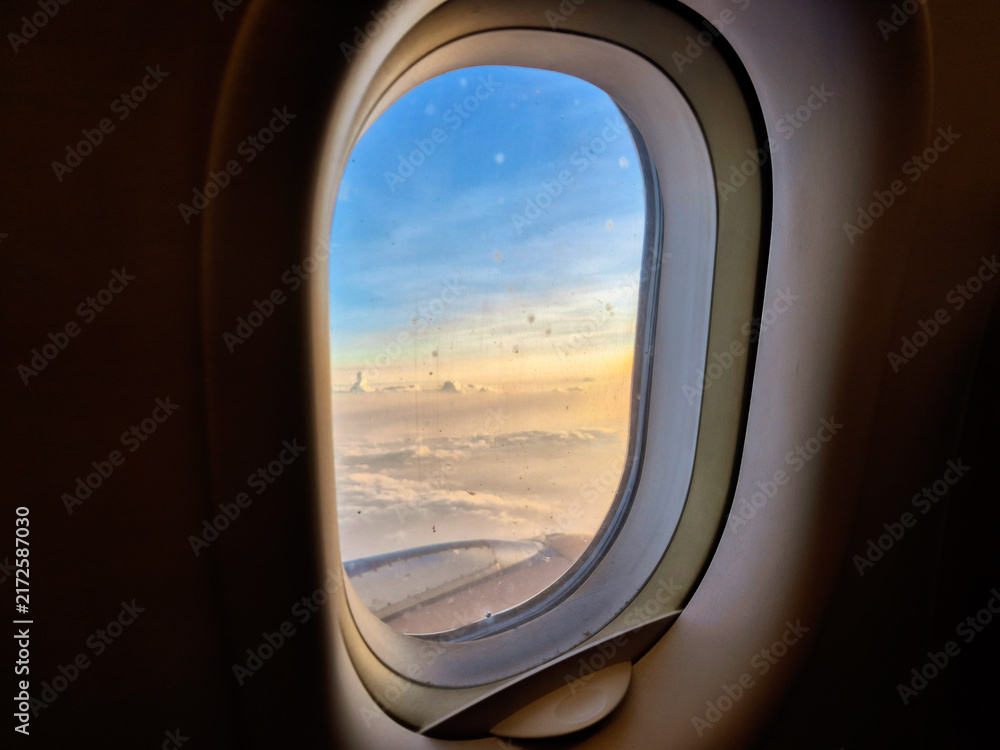 Naklejka premium View of soft clouds and blue sky during sunset from an airplane window frame, ideal for travel concept.