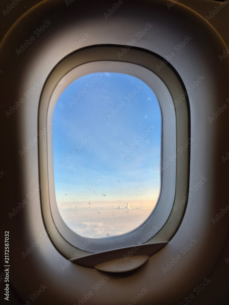 Fototapeta premium View of soft clouds and blue sky during sunset from an airplane window frame, ideal for travel concept.