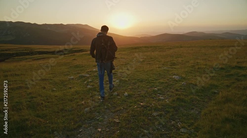 Sunset walk on a mountain trail with a person heading towards a distant horizon and trees in the background