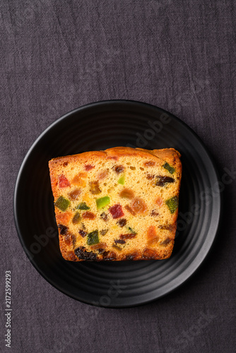 Delicious fruit cake with dried fruits served on a black plate, dark minimalist background