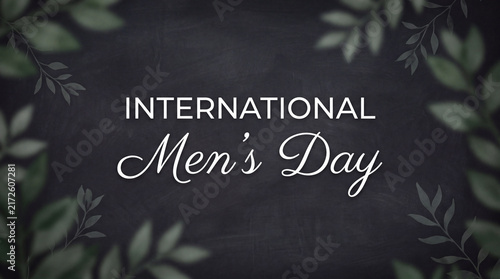 A celebratory banner for International Men's Day featuring elegant typography on a textured chalkboard background framed with decorative green leaves.