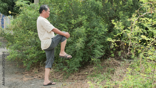 Fotografie Senior Asian man practicing knee lift leg balance exercise in park