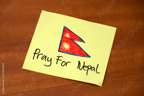 Pray For Nepal text and handwritten Nepal flag drawn on yellow sticky note on wooden background