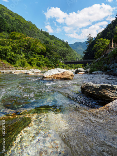 Fototapeta 青空と白い雲の下を流れる透明な清流と緑豊かな山々の夏の自然風景