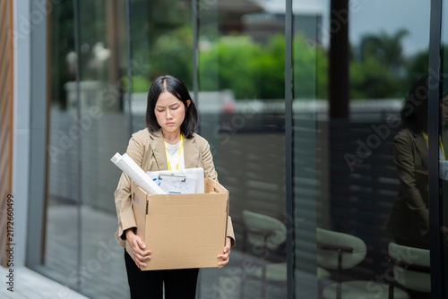 Fotografie A businessman who has lost his job walks out of the office carrying a box of his belongings, feeling sad and frustrated