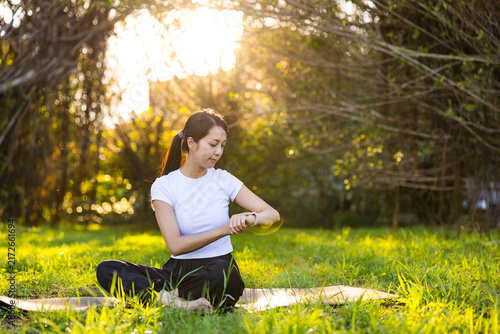 Woman sitting on a yoga mat looking down at her smartwatch in a sunny park