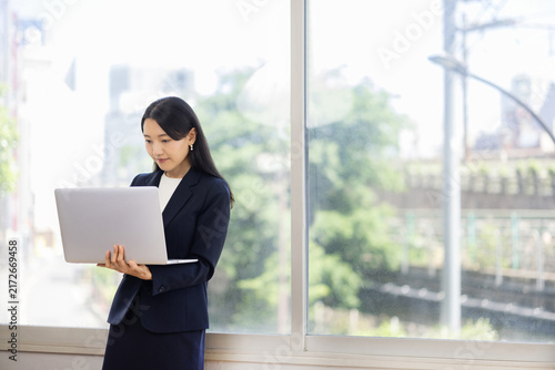 Young Japanese businesswoman working on a laptop by a bright window