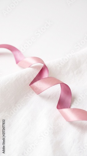 Elegant pink satin ribbon curled on white fabric with soft shadows for decoration