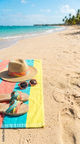 Beach scene with hat sunglasses and sandals on colorful towel by ocean shoreline