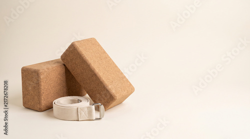 Two natural cork yoga blocks and a white cotton strap arranged on a clean beige background for a minimalist wellness concept in a professional studio photography style with copy space