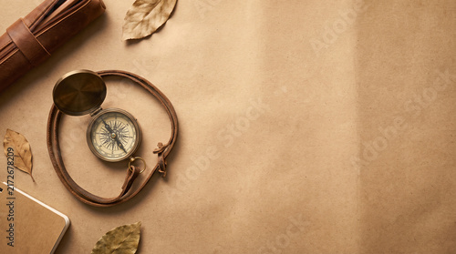 Vintage brass compass with leather strap and stationery on textured brown paper background for travel planning and exploration concept with ample copy space for commercial design