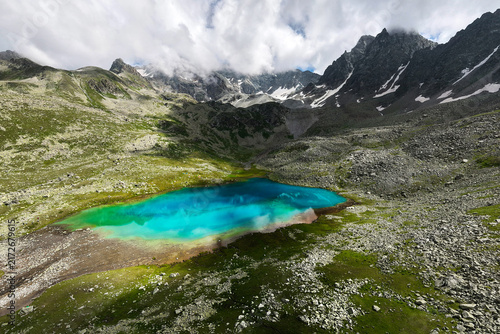 Fotografie Turquoise alpine lake surrounded by rocky mountains and cloudy sky