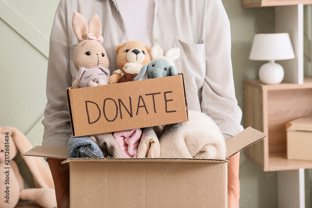 Fototapeta premium Charity donation and community support, person holding cardboard box with toys and clothes for humanitarian aid and social responsibility in home interior