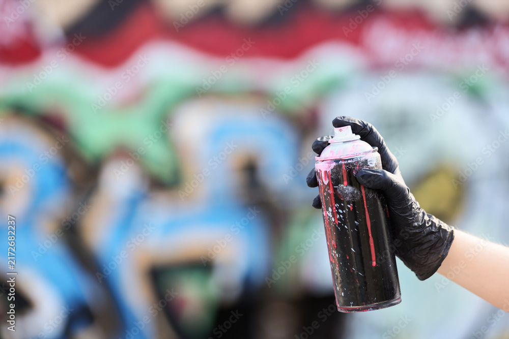 Naklejka premium Street art and urban creativity, person holding a spray paint can with black gloves in front of a colorful graffiti wall for artistic expression