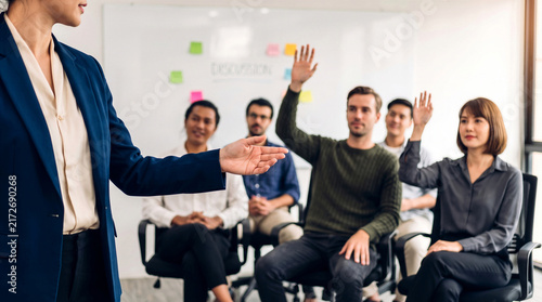 Businesswoman leading a corporate training seminar while diverse audience members raise hands to ask questions 