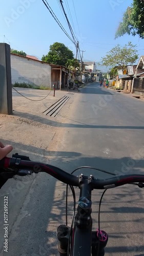 Vertical Video of Bicyclist rides down quiet residential street. Handlebars frame view of narrow road ahead. Trees cast long shadows on paved surfaces. Hand grips bike as it moves forward gently. 4K 