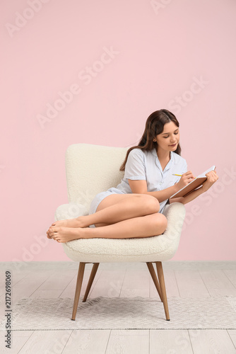 Young woman in pajamas working with tablet and sitting on armchair at home. R...