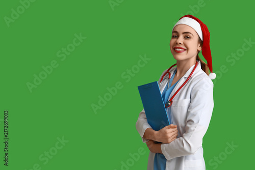 Young female doctor in Santa hat on green background