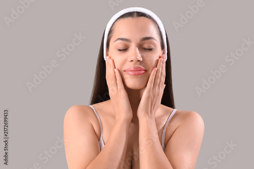 Beautiful young woman massaging her face on light background, closeup