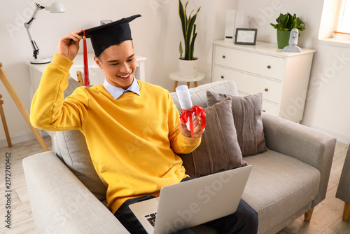 Male graduate student with diploma and laptop video chatting at home