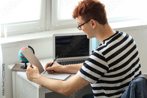 Young redhead man writing in notebook at home